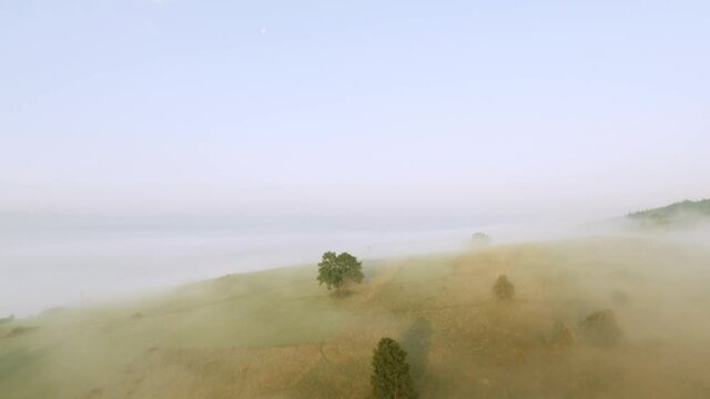 Fog around hills during a cinematic sunrise with rays of light and blue sky