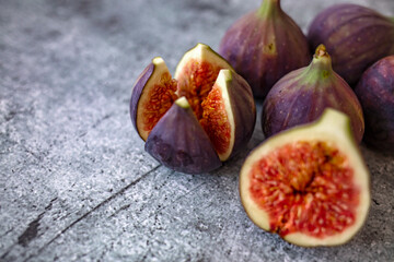 Whole figs and one fig sliced in half on top of a teak garden table. Focus is on the sliced fig. Ripe sweet figs with green leaves. Healthy mediterranean fig fruit.