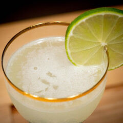 Ccoktail Lime and Gin gold rim glass with wood table background