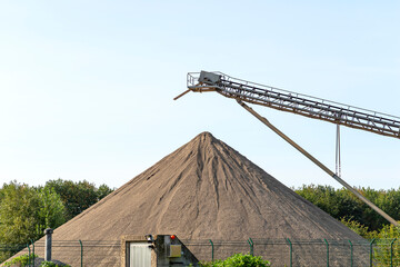 Conveyor belt over heaps of gravel against the blue sky at an industrial cement plant.