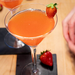 two Strawberry Cocktail in martini glass with strawberry in garnish on wood table with hand