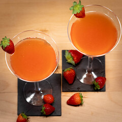 two Strawberry Cocktail in martini glass with strawberry in garnish on wood table with hand from above
