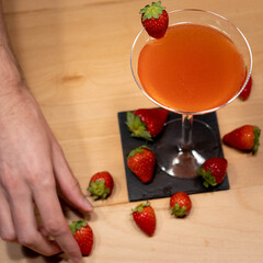 Strawberry Cocktail in martini glass with strawberry in garnish on wood table from above and with strawberries and hand