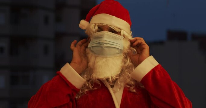 Man dressed as Santa Claus puts medical mask on his face at night in the city Christmas and coronavirus