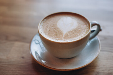 One cup of cappuccino with latte art on wooden table, white ceramic cup, place for text. Cafe culture.