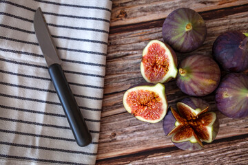Fresh ripe figs on table background. Healthy Mediterranean fig fruit. Beautiful blue-violet figs with empty copy space close up. Whole figs and one fig sliced in half on top of a teak garden table. Fo