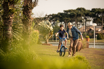 Obraz premium Avô ensinando neto andar de bicicleta no jardim.