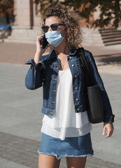 Curly hair woman in mask works on mobile phone outdoors