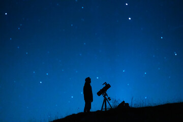 Astronomer observing the immensity of the universe and the stars. Silhouette of a astronomy lover person with a telescope observing the blue starry sky at night.
