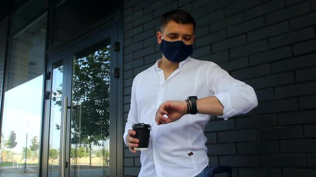 Men in protective mask with a coffee looks at watch.