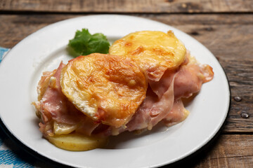Scalloped potatoes with ham and cheese on wooden background