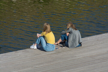 girls sit on a wooden embankment and look at the water