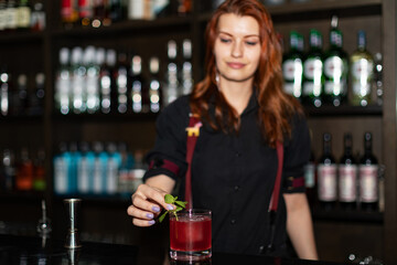 Bartender pouring cocktail from shaker into glasses at bar counter in bar, focus on coctail