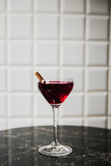A deep red cocktail in a nick and nora glass garnished with cinnamon