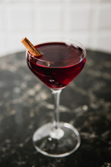 A deep red cocktail in a nick and nora glass garnished with cinnamon