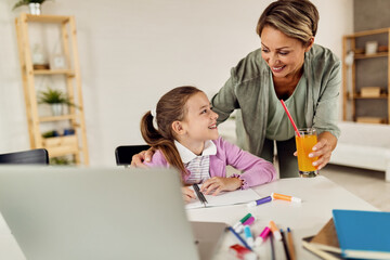 Happy mother giving refreshment to her daughter who is writing a homework.