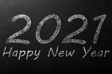 The inscription Happy New Year 2021 in white chalk on a dark blackboard.
