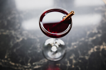 A deep red cocktail in a nick and nora glass garnished with cinnamon