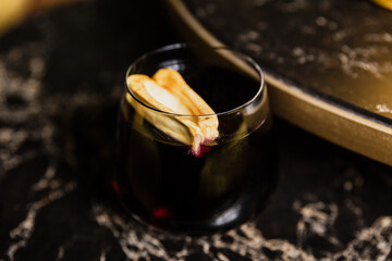 A dark colored cocktail in a rocks lowball glass garnished with a dried fruit