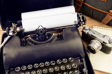 an old 1940s black portable typewriter with a 35 mm film camera and a notebook suggesting a  travel...