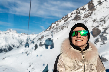 Young adult beautiful happy attractive caucasian smiling woman enjoy ascent sitting inside ski lift gondola cable car against skiing resort panorama breathtaking view. Winter travel welcome concept