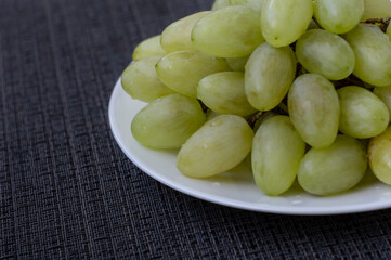 White sweet grape in the white plate on dark black surface