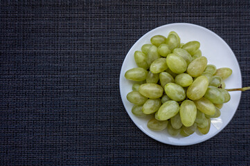 White sweet grape in the white plate on dark black surface
