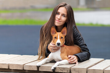  'Portrait of beautiful young woman with her purebreed basenji Congo terrier dog. Girl is hugging her puppy and looking at camera