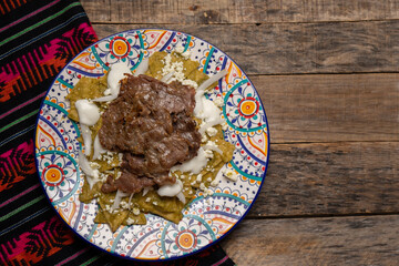 Mexican green chilaquiles with cecina beef steak on wooden background