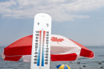 A Canadian flag umbrella at the beach on a hot day with a thermometer showing about 90 degrees...