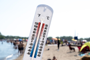 A thermometer held up over a a hot crowded beach, reading about 90 degrees Fahrenheit 30 degrees...