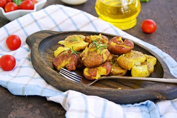 Crash Hot Potatoes, boiled potatoes in a peel, crushed and baked with olive oil and herbs on a wooden plate on a dark concrete background. Australian cuisine. Potato recipes.