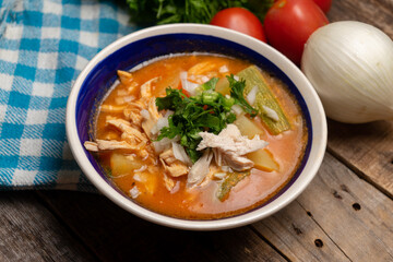 Mexican chicken soup with vegetables and rice on wooden background
