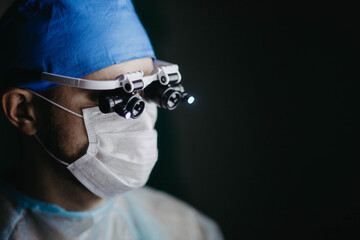neurosurgeon wearing binocular magnifying glasses operates on a patient in a dark operating room