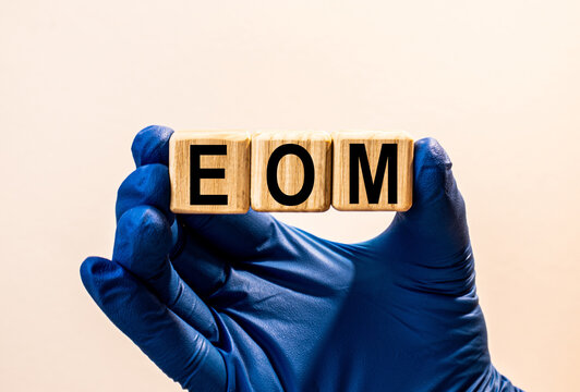 The word EOM which is made from wooden cubes. Hands in a blue glove. Isolated on WHITE background.