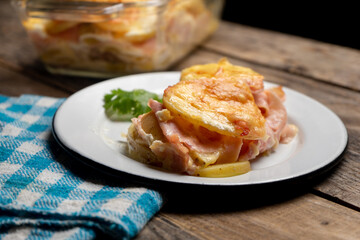 Scalloped potatoes with ham and cheese on wooden background