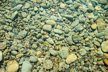Large pebbles under water on The black sea coast. Splashes and sun glare.