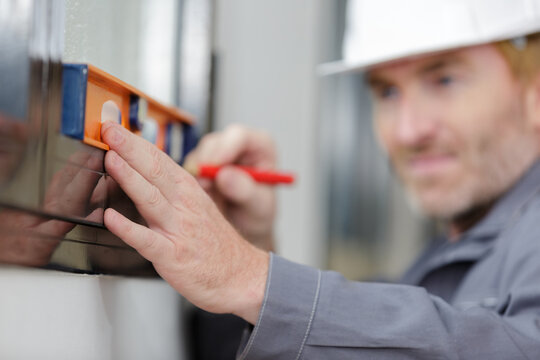 man measuring wooden wall with level and pencil