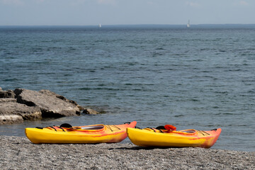 two colorful one person kayaks drawn up on a rocky beach by a lake