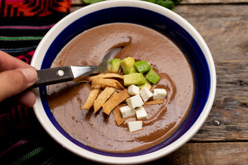 Mexican cream of bean soup with avocado and cheese on wooden background