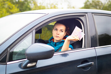 Serious woman holding out driver's license and car documents, driving her car. Traffic violation concept, stop, document check