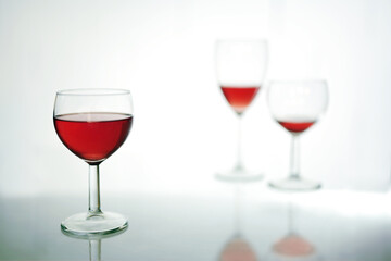 Drinking glass with red wine in the foreground, two more blurred further back, light gray blue background with copy space, selected focus
