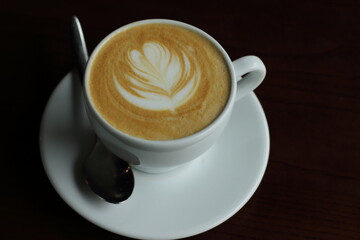 Coffee with foam in white cup in black light, dark background, flower foam on top 