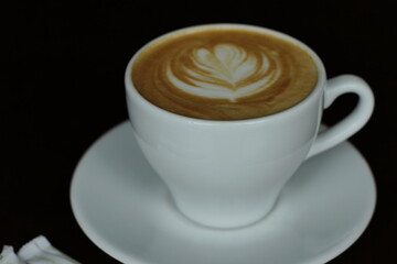 Coffee with foam in white cup in black light, dark background, flower foam on top 