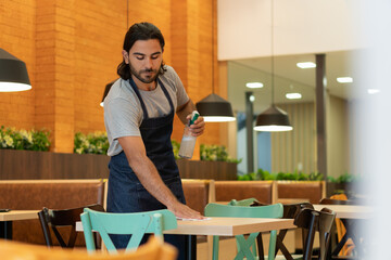 Serious latin male professional with cleaning cloth cleaning workplace inside business store....