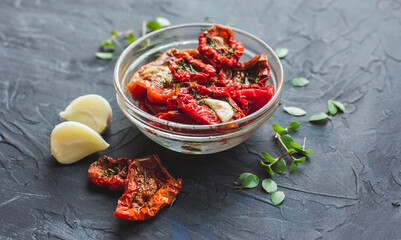 Dried tomatoes with garlic and olive oil in a bowl on a gray table background