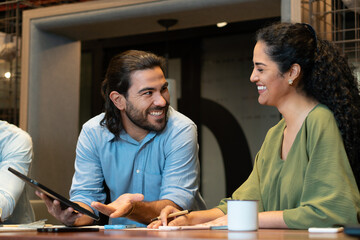 Cheerful latin business colleagues with tablet collaborating and discussing project plans open office space. Unity, teamwork, collaboration concept..