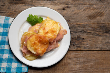 Scalloped potatoes with ham and cheese on wooden background