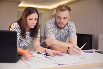 two young people, studying together, sitting in front of notes on a desk.