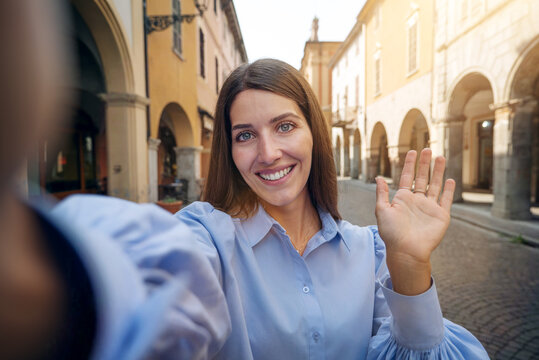 Authentic Shot Of Young Happy Carefree Woman Is Making Selfie Or Video Call To Her Boyfriend Or Parents In Old City Center In A Sunny Day. 